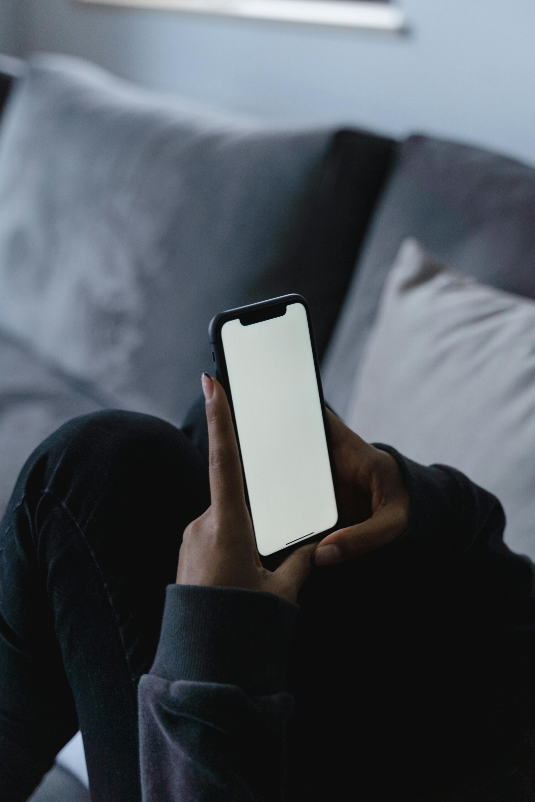 Close-up of a smartphone with a blank screen being held by a person on a couch.